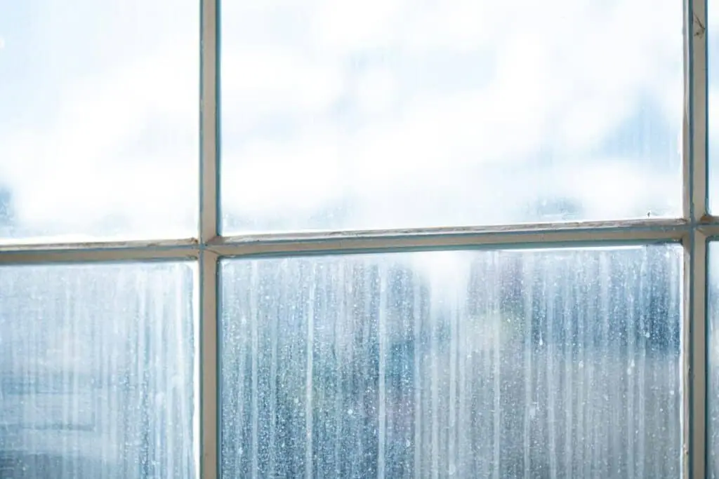 A streaked, rain-marked multi-pane window seen from inside against a bright sky